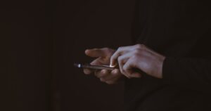 Χέρια κρατούν κινητό τηλέφωνο σε σκοτεινό φόντο.